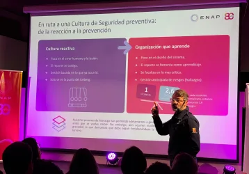 Iluminación Corporativos - FBAudio – Pantallas Led – Streaming – Amplificación Speaker presenting a slide in a dark auditorium with pink lighting; slide has purple and pink panels titled 'Cultura reactiva' and 'Organización que aprende'.