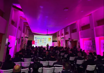 Iluminación Led para eventos corporativos - FBAudio – Pantallas Led – Streaming – Amplificación Conference hall with purple lighting, audience seated and facing a presenter at the front with a projected slide
